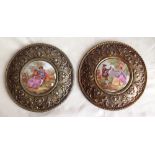 A pair of metal wall plaques with central porcelain panels depicting French 17th century courting