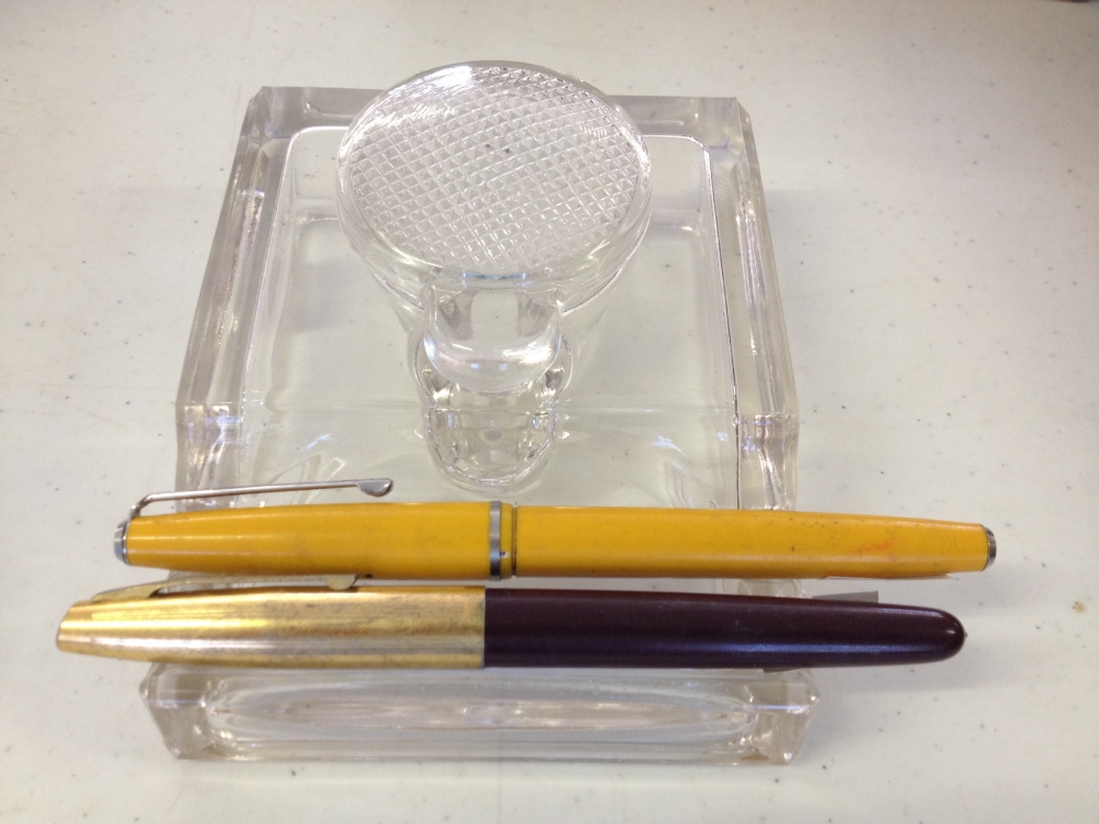 A glass inkwell with a yellow Platignum 'Silverline' fountain pen, and another unmarked fountain