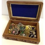 A carved wooden box containing vintage brooches including silver.