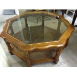 A large octagonal glass topped coffee table with cane shelf approx 108cm diameter.