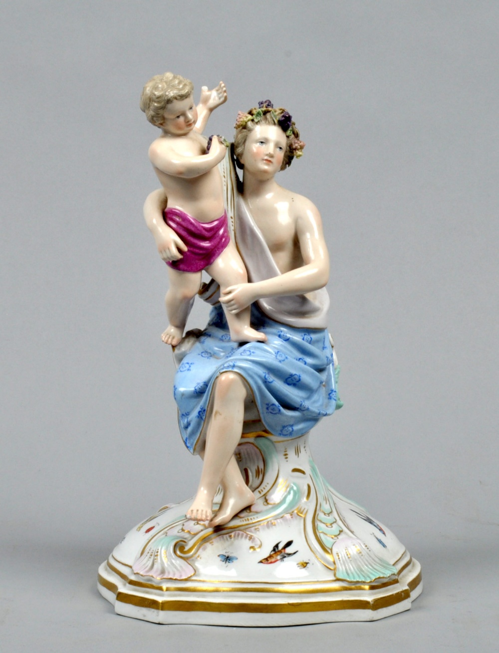 A 19c Meissen figure group being a young man seated on a shell and supporting a putto on his knee,