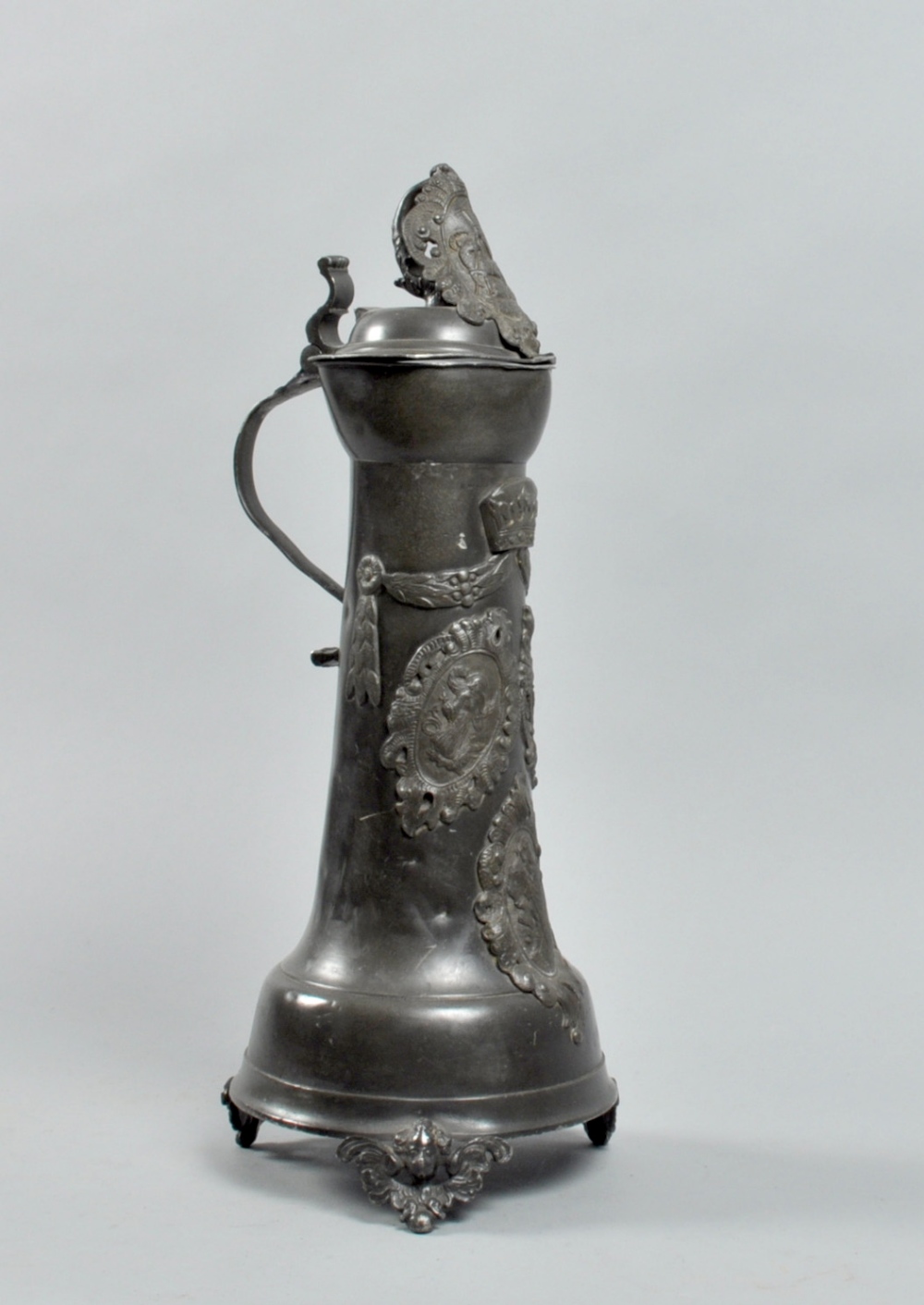 A 19c German pewter flagon decorated with heraldic crests, swag and crown, having a hinged domed