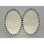 A pair of oval wall mirrors with blue, white and gilt glass chequer borders, each 18" x 26.5".