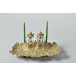 A Victorian brass two bottle inkstand, rococo cast and having two clear glass moulded bottles (one