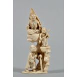 A Meiji period carved ivory okimono of a devil figure with a chained guard seated and standing on
