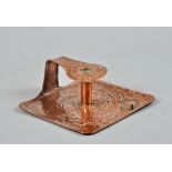 An Art Nouveau copper chamberstick in the style of Newlyn, having a square base with raised