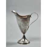 A late 18c cream jug of helmet shaped form, with scrolling handle, on a circular tapering base,