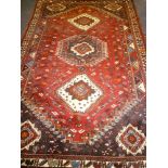 An Eastern-style hand knotted wool rug with geometric decoration on red ground 112" x 72"