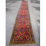 An old Eastern hand knotted wool runner with geometric and floral decoration on red ground, 210" x