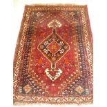 An Eastern hand knotted wool rug with geometric decoration on red ground 64" x 46"