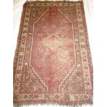 An old Eastern hand knotted wool rug with geometric decoration on red ground 61" x 42"
