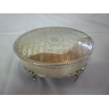 A George V silver oval jewellery box with engraved hinged lid on four scroll feet, Birmingham