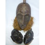 An old African carved wood mask with protruding nose and raffia collar together with two smaller