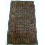 An old Eastern hand knotted wool rug with geometric and floral decoration on red ground 58" x 35"