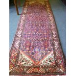 An Eastern hand knotted wool runner with geometric floral decoration on red and blue ground 131" x