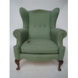 A late Victorian wingback armchair, with scroll arms, raised on squat cabriole forelegs,