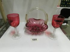 A pair of cranberry glass wine glasses with cut glass stems and a cranberry glass basket