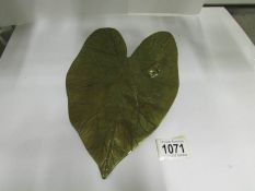 A brass wall plaque in the shape of a lily pad with a frog and an insect
