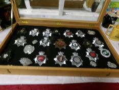 A display case containing 23 police helmet badges and one vintage Worcestershire regiment helmet