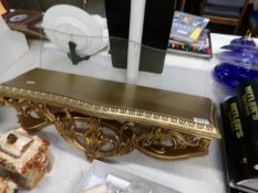 A gilded wall shelf with glass top