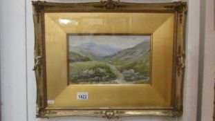A gilt framed watercolour of sheep in a mountain valley