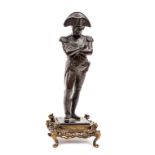 A bronze figure of Napoleon, wearing bicorne hat, standing with arms folded, his right foot