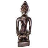 An early 20th century Kongo hardwood kneeling female maternity figure from the Congo, holding a