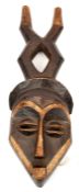 An African carved wood mask,  with angular features and slit eyes, darkened with the eyebrows,