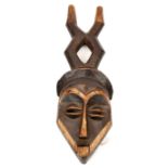 An African carved wood mask,  with angular features and slit eyes, darkened with the eyebrows,