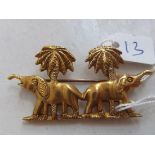 A high carat gold double elephant brooch standing under palm trees 2” wide 14.8g