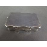 A silver pill box of shaped form with a