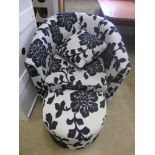 A modern tub armchair upholstered in foliate design with matching footstool