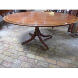 An oval crossbanded dining table raised on swept quatrefoil base terminating in brass feet with