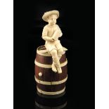 λ A late 19th century German carved ivory group of a young boy, seated on a barrel holding a