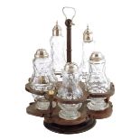 A George III treen lignum vitae cruet, with five cut glass bottles with silver plated lids, with