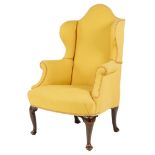 A wing armchair in Queen Anne style, with scroll arms and on ebonized cabriole front legs and pad