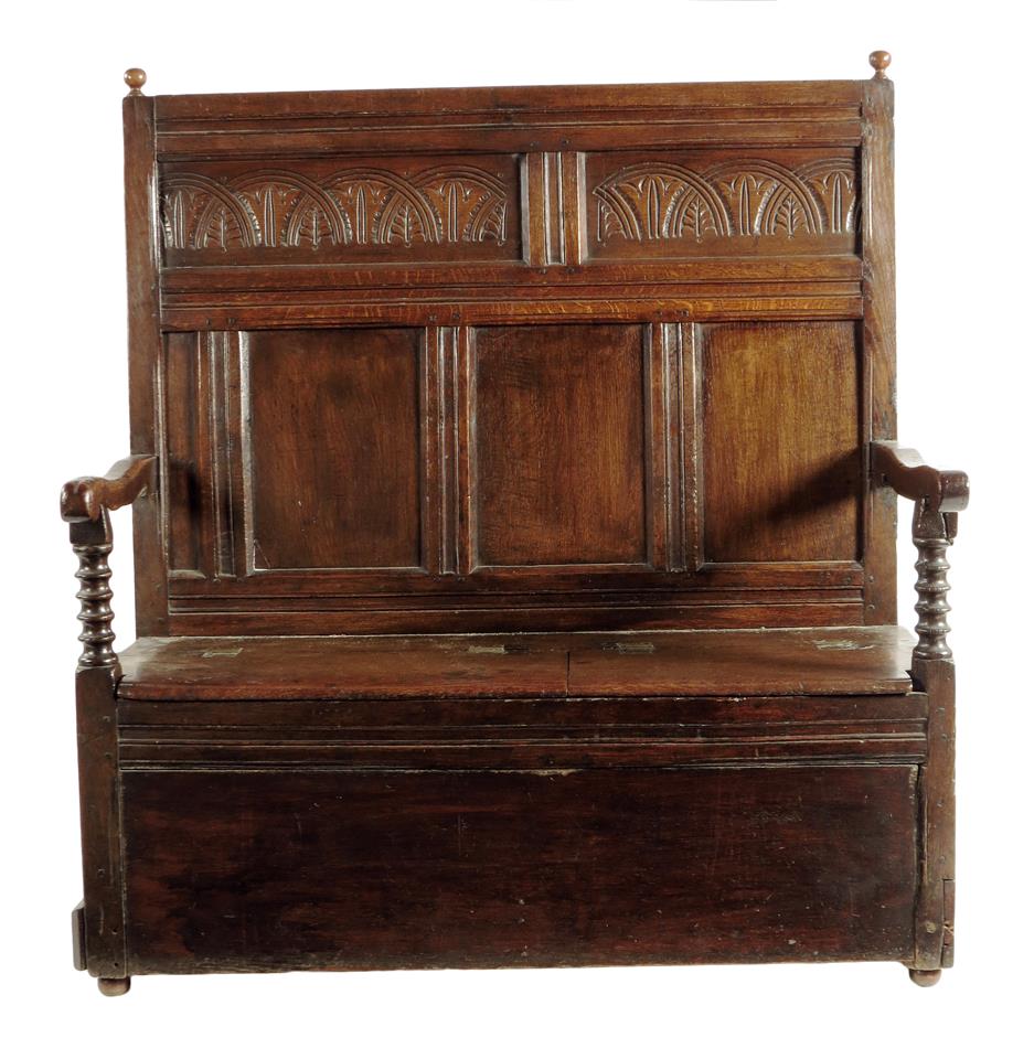 An oak settle, the panelled back carved with foliate lunettes above a twin hinged box seat, with