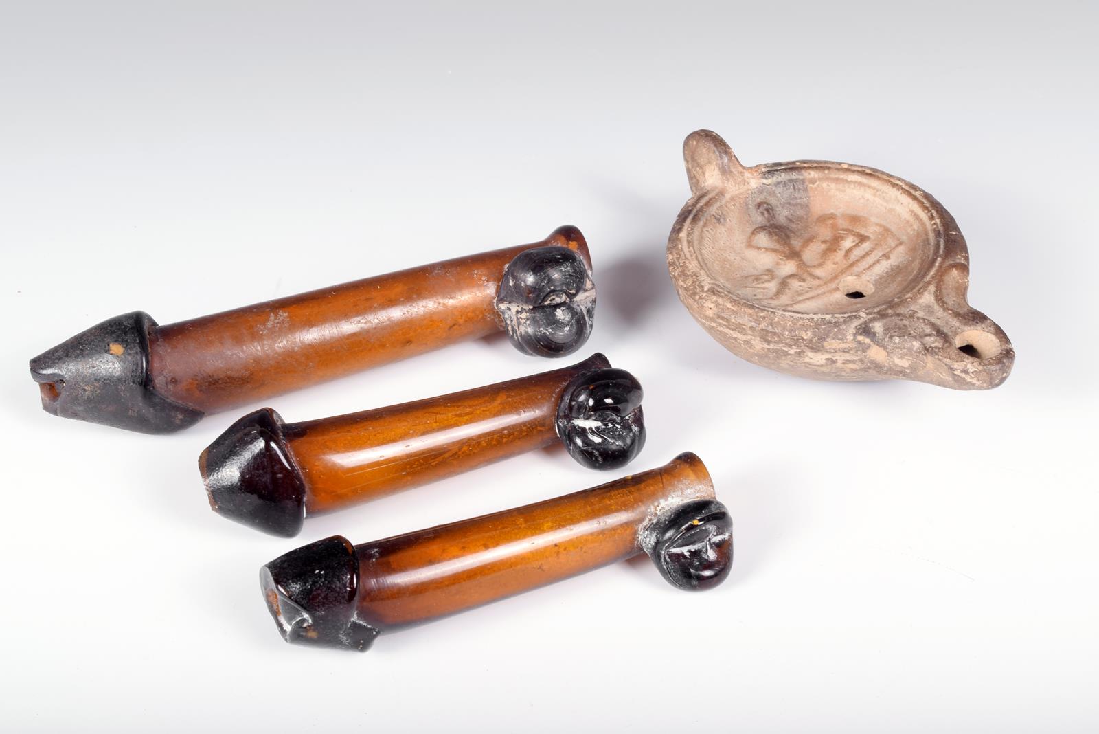 A Roman pottery oil lamp, the centre moulded an erotic scene, 10.5cm long and three glass phallic