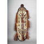 A Papua New Guinea ancestor board, carved masks and with fibre adornment, 87cm high.