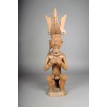 A Nias seated ancestor figure, Indonesia, with elaborate headdress, one earring and holding bowl,