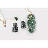 A Maori nephrite pendant, of an S scroll with two tiki masks, 7.5cm long, with a cord and nephrite