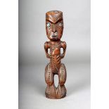 A Maori carved wood standing tiki, holding a patu and with inlaid shell eyes, 28cm high.