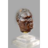 A Maori kauri gum portrait head, with incised moko ornament to the face, 7.2cm high, on a perspex