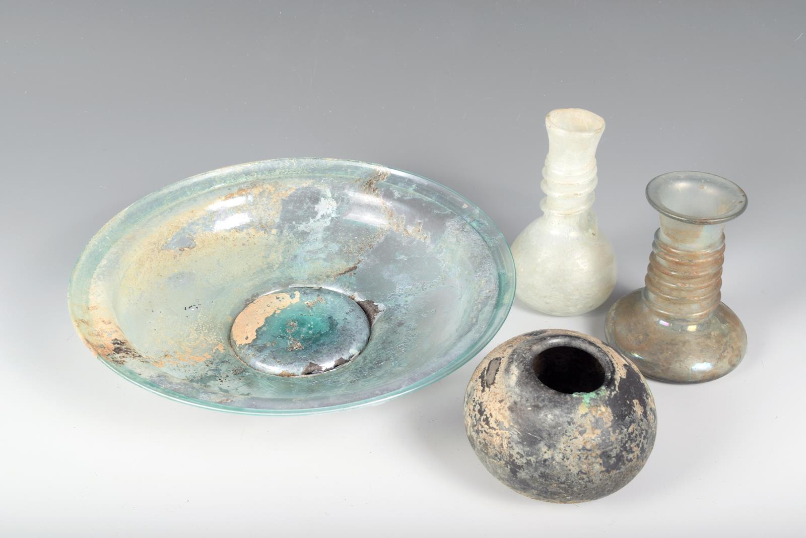 A Roman glass circular dish, on a spreading foot, 21.5cm diameter, two glass vessels with spiral