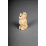 λ An Inuit carved bone seated figure of a stargazer, looking upwards with darkened features, with