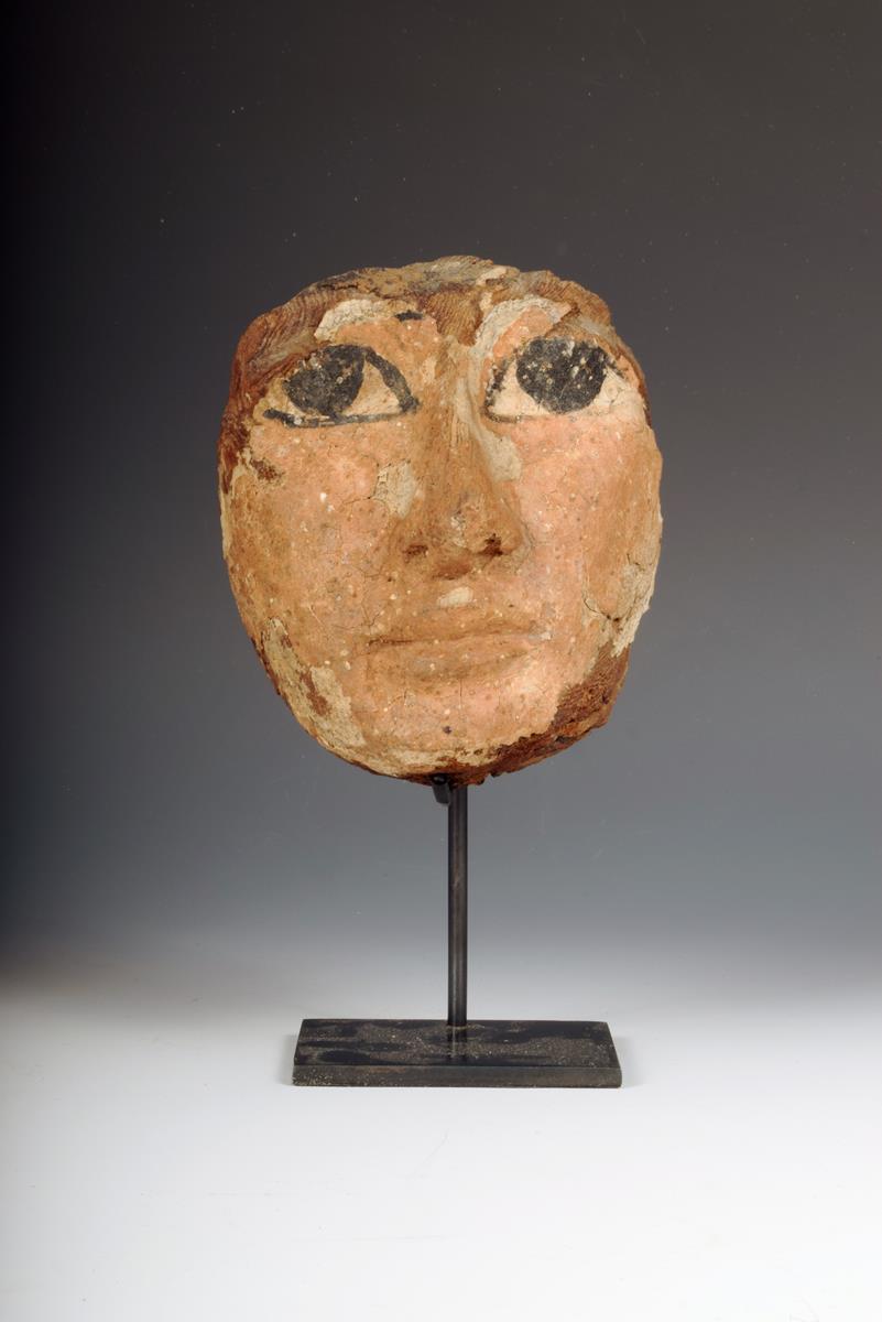 An Egyptian carved wood mask, with polychrome decoration, 13cm high, on a stand. (2)