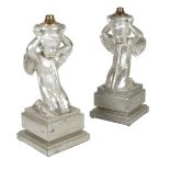 A pair of silvered tin cherub lamps, the winged figures kneeling on a square stepped plinths, 77.3cm