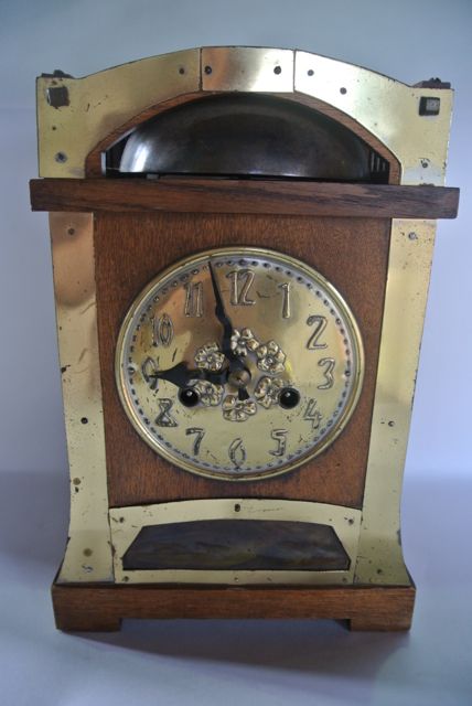 An Arts & Crafts mantle clock in oak with applied brass detail, with embossed brass dial over a