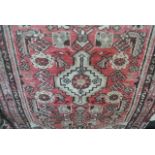 A small wool carpet in the Persian style with red ground field, geometric detail, set within running