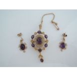 A pair of 9ct gold stud earrings, each suspended with a cabochon amethyst within a scrolling border;